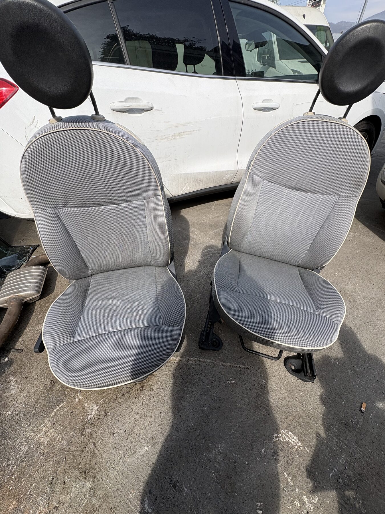 Due sedili anteriori in tessuto grigio smontati dall'auto e appoggiati sul piazzale