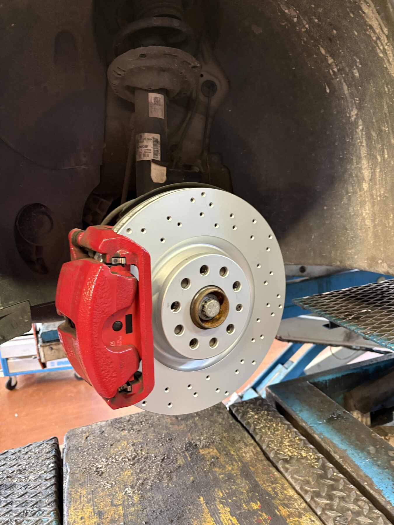 Pinza freno verniciata di rosso e disco forato, con l'auto sollevata sul ponte dell'officina