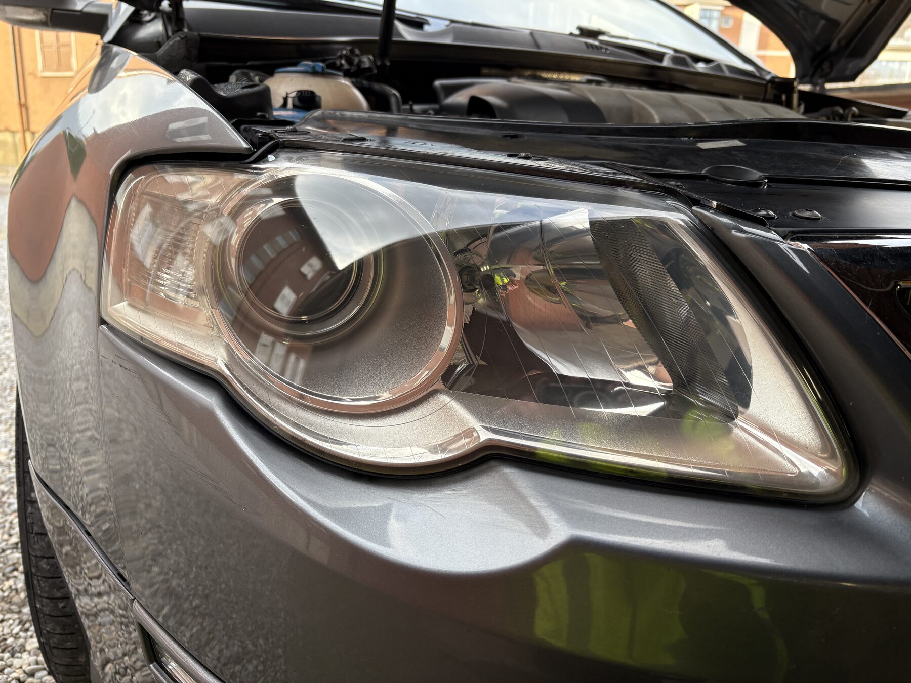 Faro anteriore limpido di una berlina grigia, con il cofano sollevato