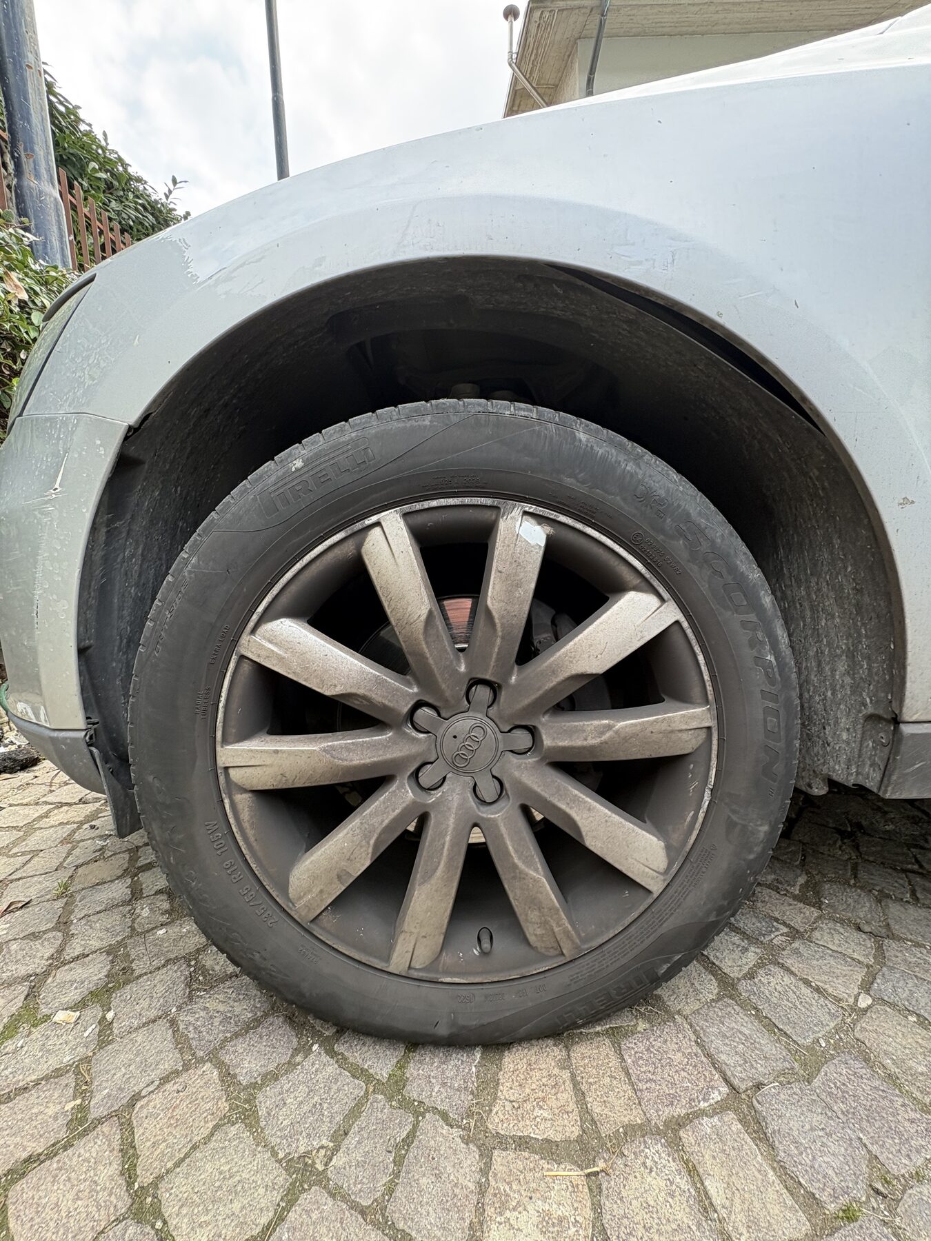 Ruota di un SUV grigio chiaro con cerchio a razze, su un piazzale in pietra