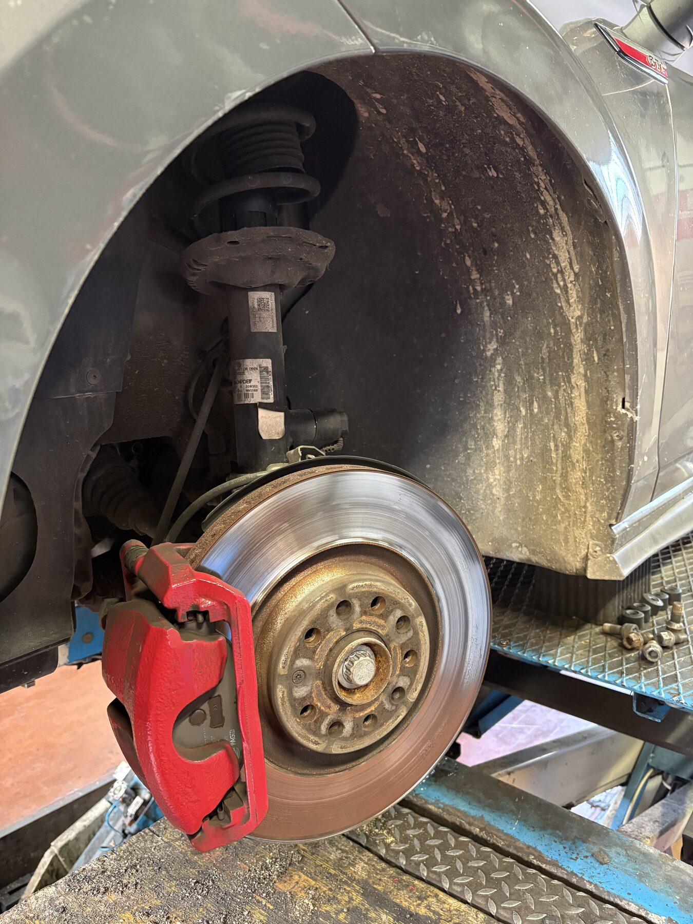 Pinza freno rossa e disco forato visti dal passaruota, con l'auto sul ponte